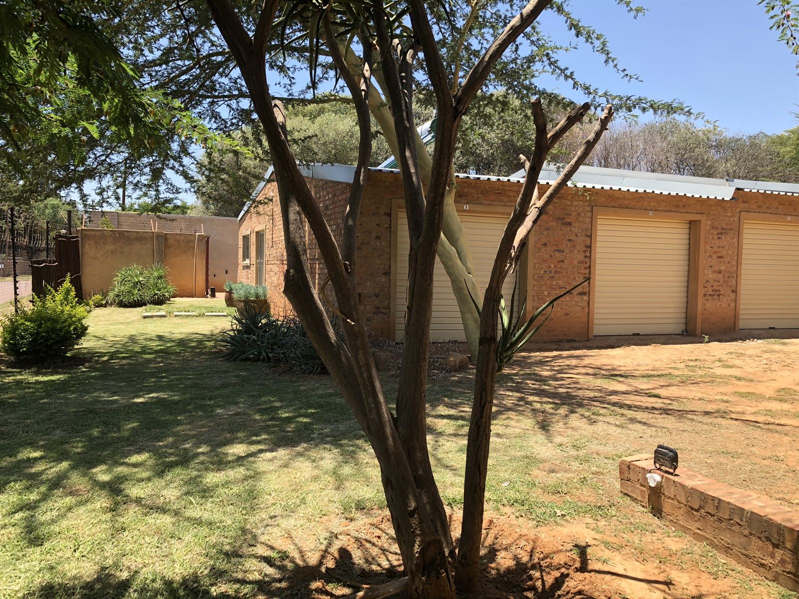 Storage garages set on a mown lawn beside a walled, electric-fenced boundary