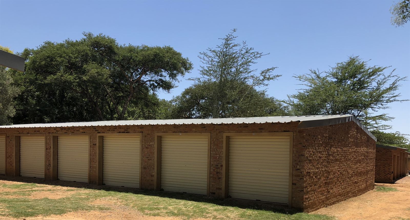 Block of storage garages on a green lawn with trees behind