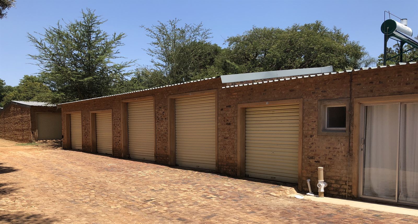 Paved driveway alongside a row of brick garages with cream roller doors